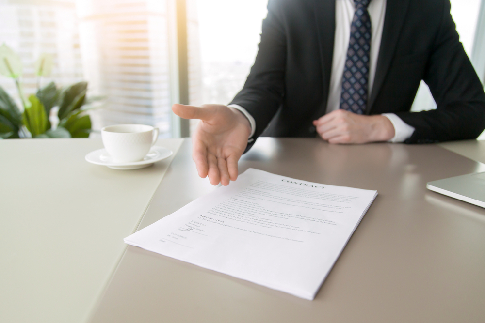 man in suit gesturing to paper with coffee cup on desk